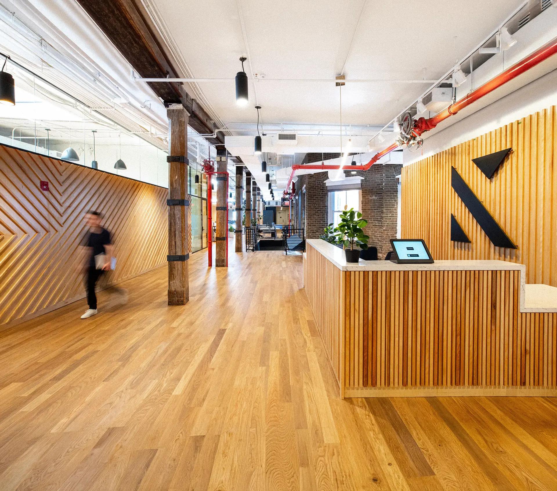 Konrad office reception with wood-slat walls, exposed brick and the angular Konrad logo behind the desk