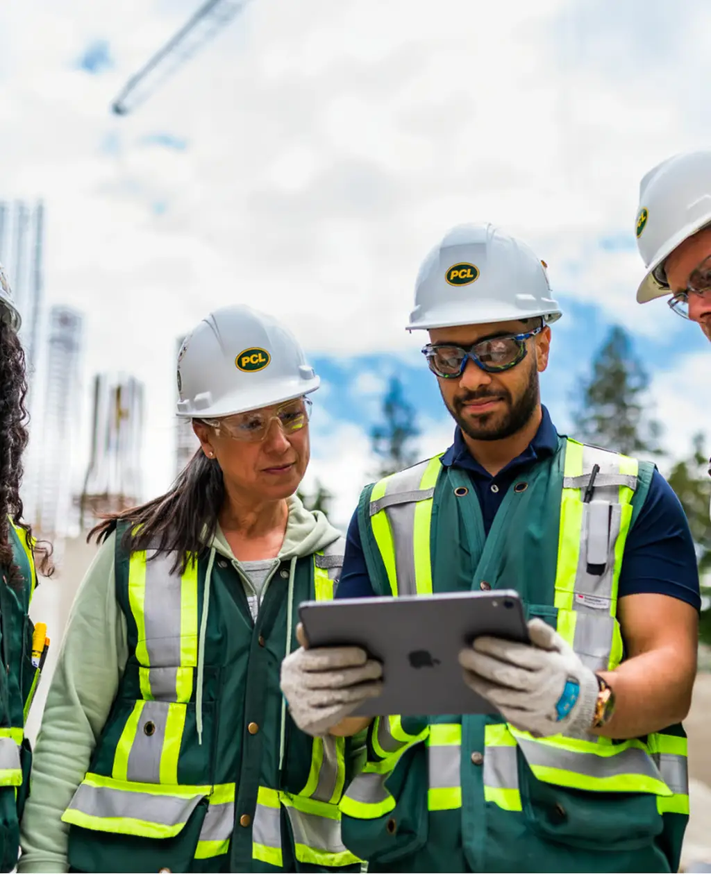 Two workers in hi-vis vests and hard hats reviewing plans on a tablet at a construction site