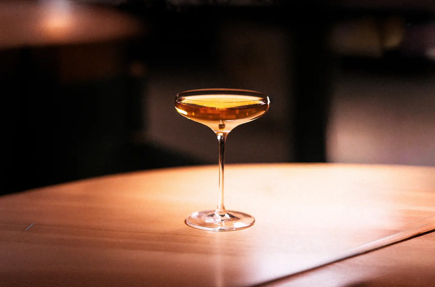 Amber cocktail in a coupe glass, lit warmly against a dark background