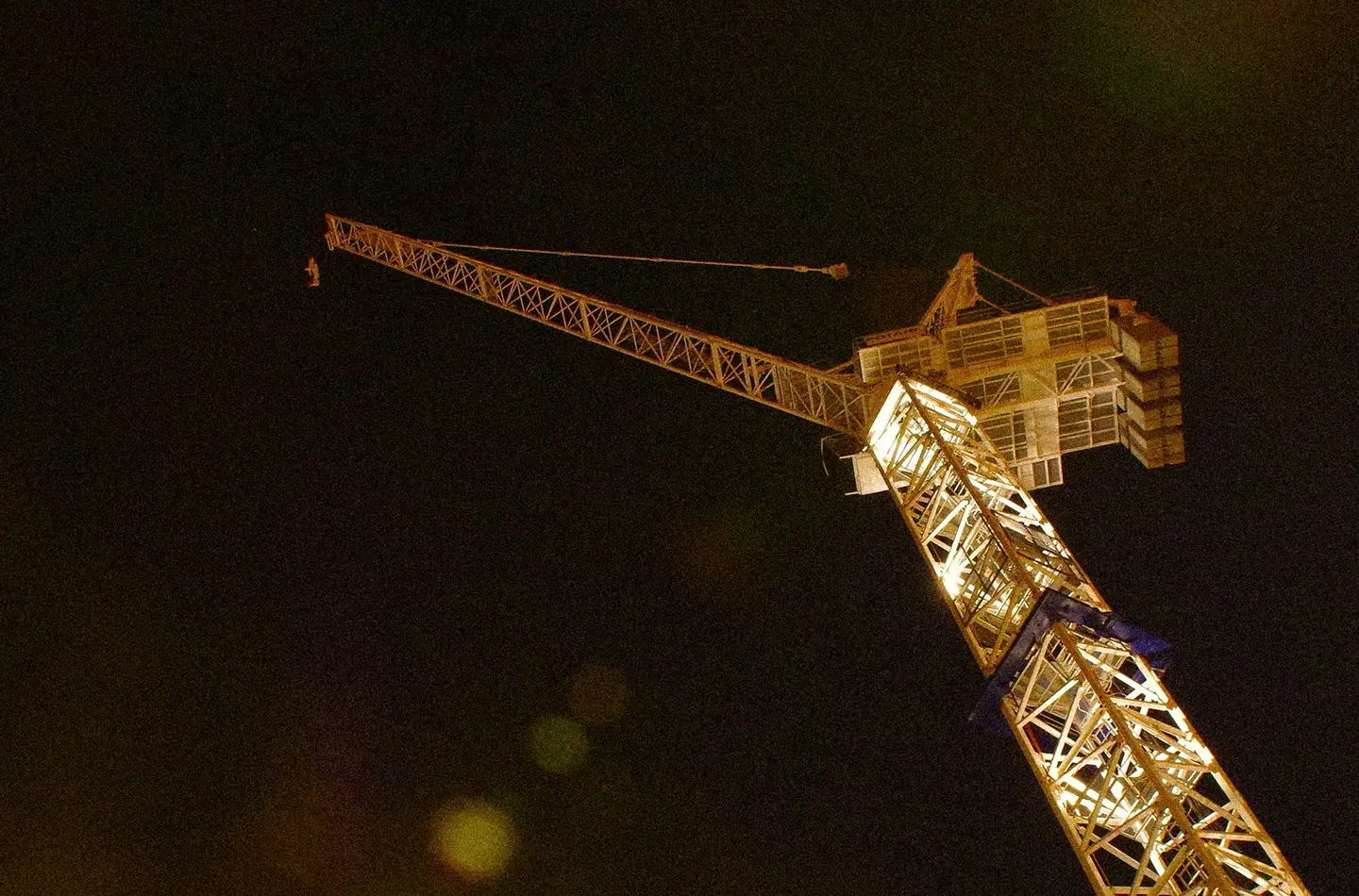 Construction tower crane lit up against a night sky, seen from below