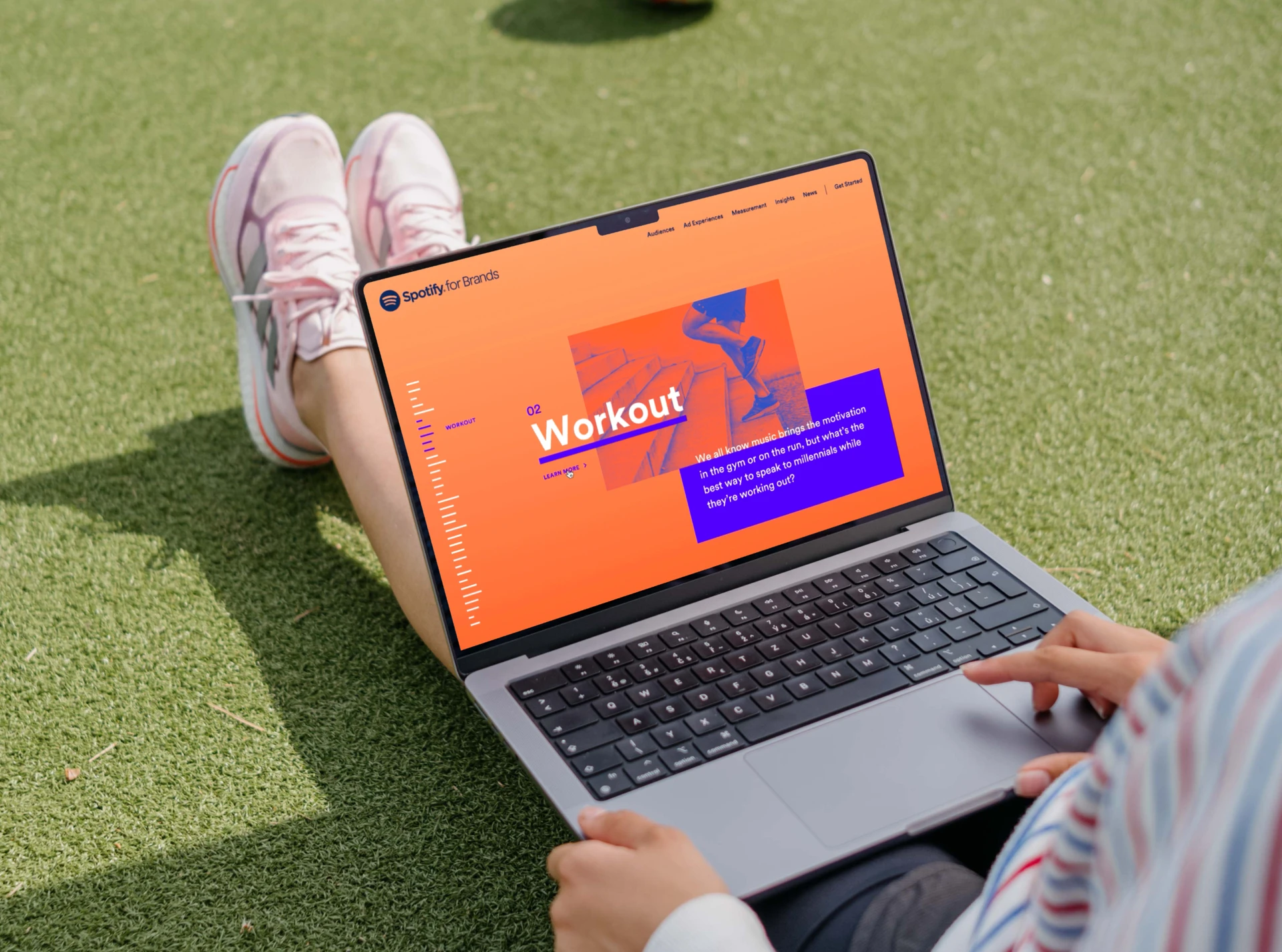 Person sitting on a lawn with a laptop open to the Spotify for Brands “Workout” page