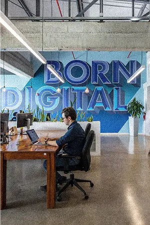 A team member working at a laptop in front of a blue “Born Digital” mural